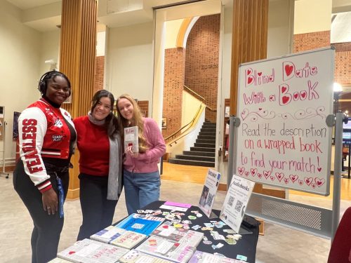 3 Students pose infront of a table of books at the Blind Date with a Book event at ZSR Library. 