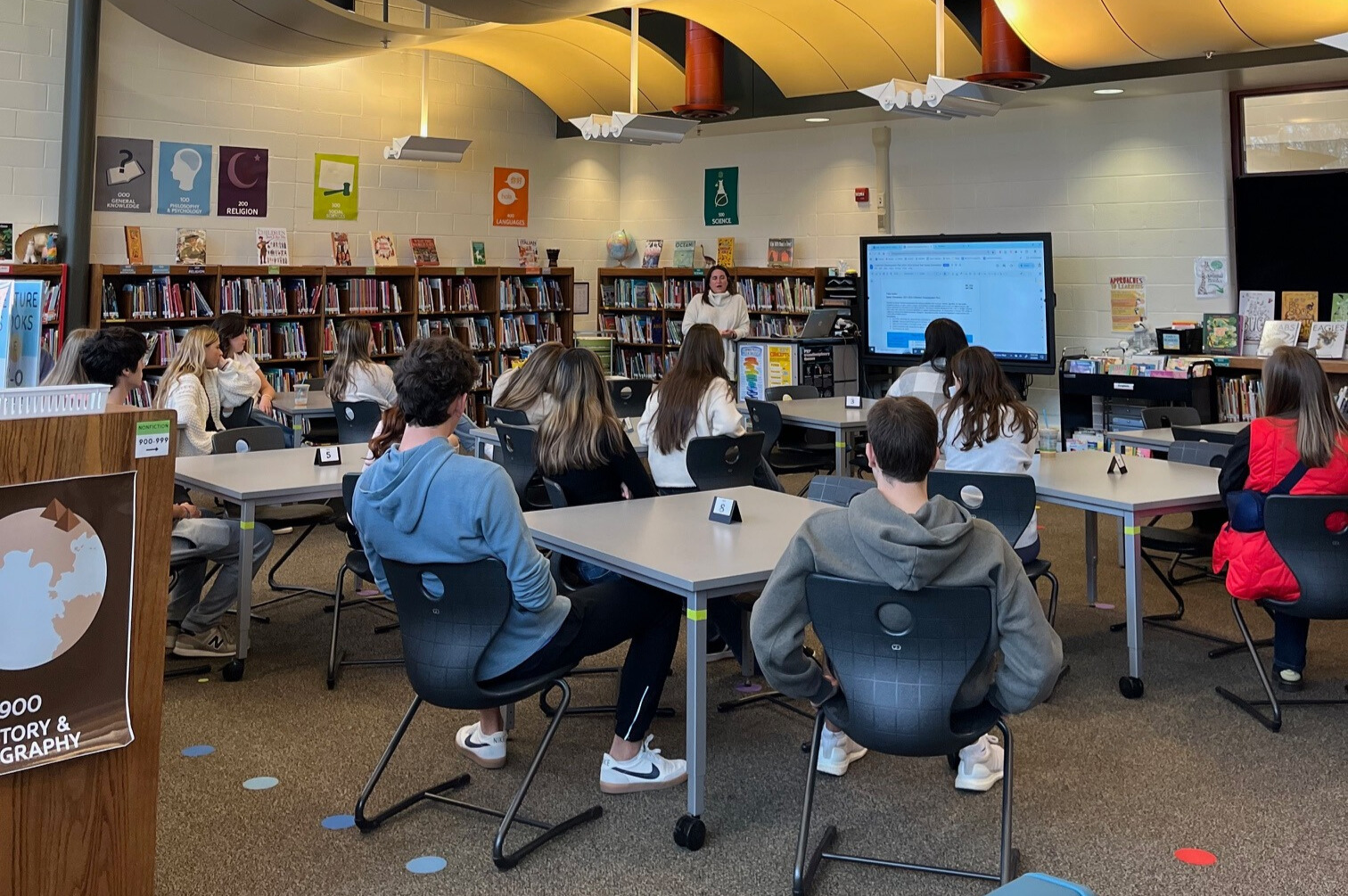 students sit in school library listening to librarian 