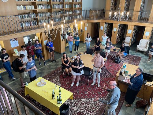 A group of students and library faculty gather in the Special Collections and Archives reading room. Some hold glasses of sparkling cider, while others peer at the Persian rug and bookshelves ornamenting the room