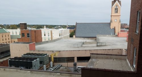 View taken from the sixth floor of a hotel shows an attractive church steeple, but also the ugly roof of a parking deck.