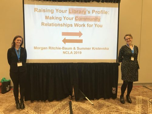 Summer Krstevska and Morgan Ritchie-Baum standing in front of their presentation title slide that is being projected in a conference room at NCLA Conference 2019