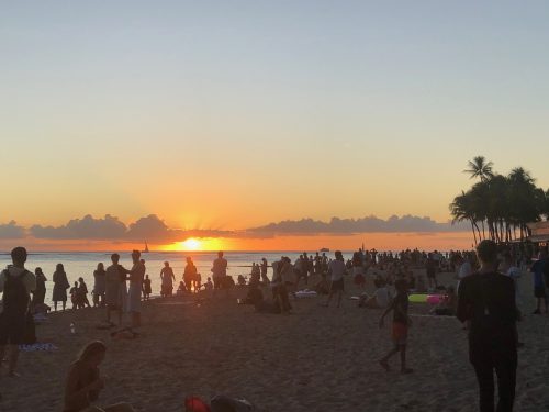 A beach at sunset, crowded with people