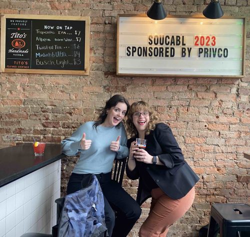 Two women smile at the camera in a bar. 