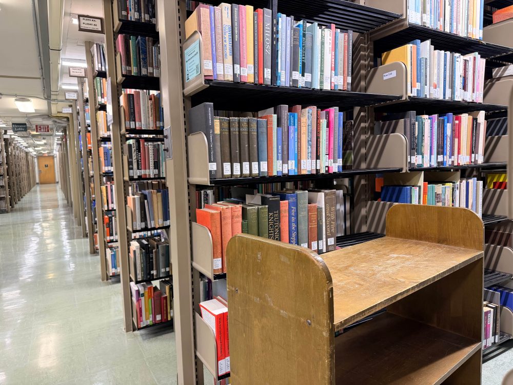 Library aisle on Reynolds 5 of ZSR Library with a wooden book truck in front of shelves filled with books.