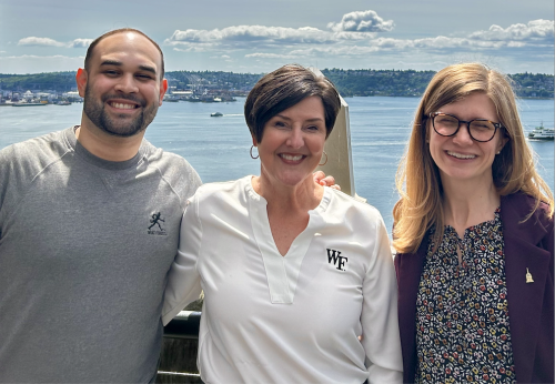 Three people, smiling, on a rooftop with Puget Sound in the background.