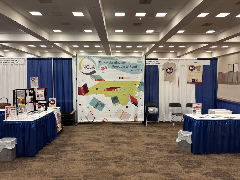 A conference booth with materials across two tables and a branded photo backdrop.