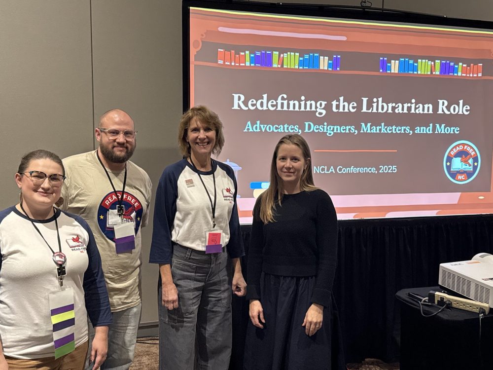 Four people standing in front of a screen with a presentation displayed.