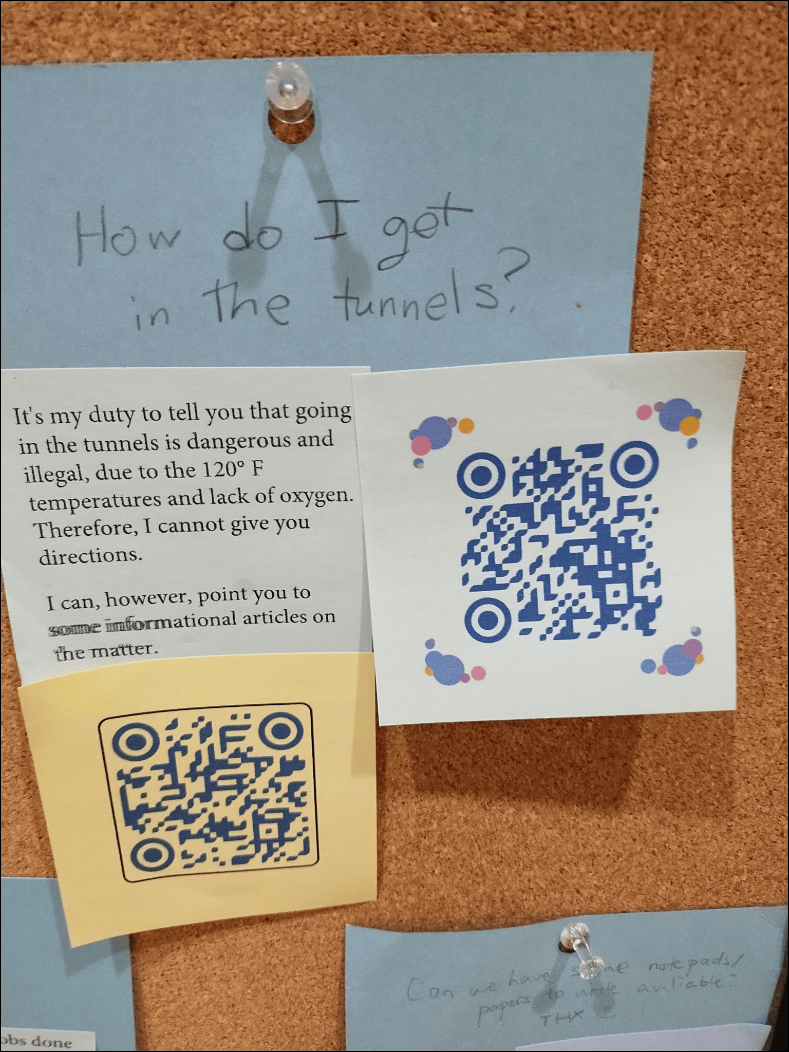 A bulletin board with various pinned notes and QR codes. A handwritten note on blue paper at the top reads, “How do I get in the tunnels?” Below it, a printed note says, “It’s my duty to tell you that going in the tunnels is dangerous and illegal, due to the 120°F temperatures and lack of oxygen. Therefore, I cannot give you directions. I can, however, point you to some informational articles on the matter.” Two QR codes are visible, one on yellow paper and one on white paper with colorful dots.