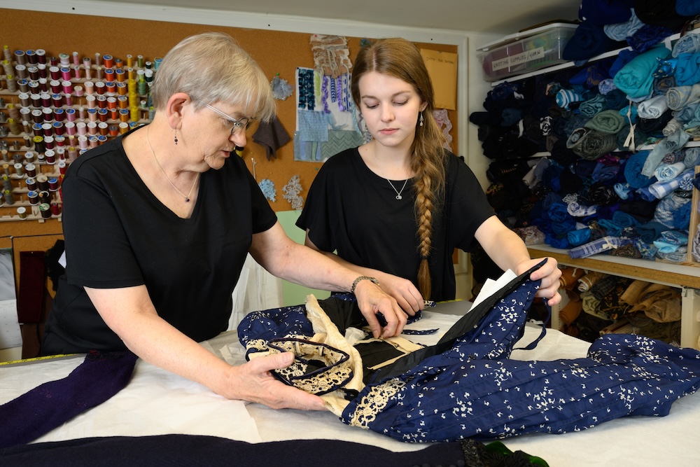 Two women examine a vintage blue coat laid flat on a table